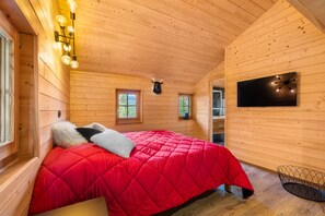 A cozy wooden cabin bedroom with a red bedspread, two windows, a mounted TV, and a ceiling light fixture. - Laetitia Chalet - Sleeps 8 - Charm and Authenticity (Haute-Nendaz)
