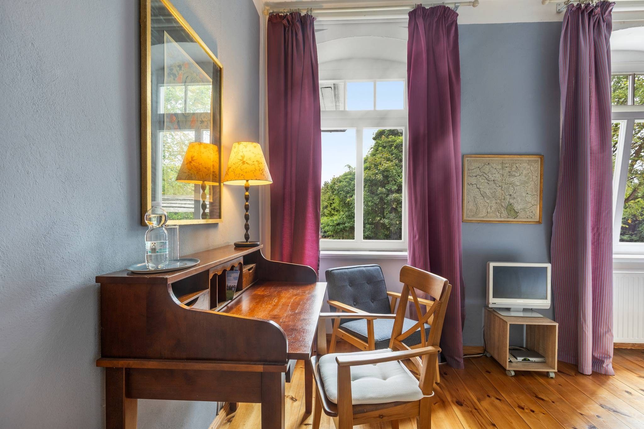 A dining area with a wooden table, chairs, a lamp, a television, and a window with curtains.