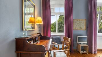 A dining area with a wooden table, chairs, a lamp, a television, and a window with curtains.
