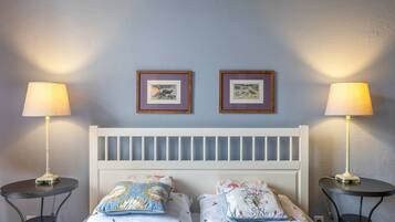 A bedroom with a white headboard, two bedside tables with lamps, and two framed pictures on the wall.