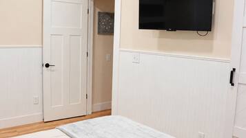A bedroom with a bed, a ceiling fan, a television mounted on the wall, and a door leading to another room.