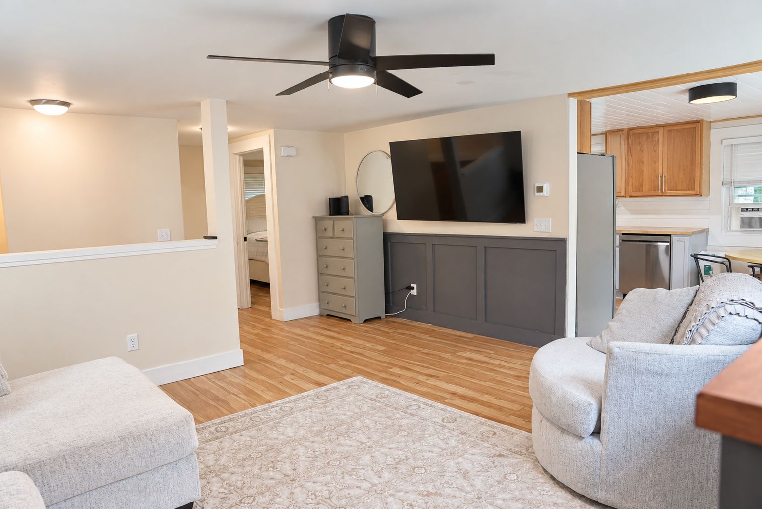 Un salon moderne doté d’un ventilateur de plafond, d’un téléviseur à écran plat, d’un canapé gris et d’un plancher en bois.
