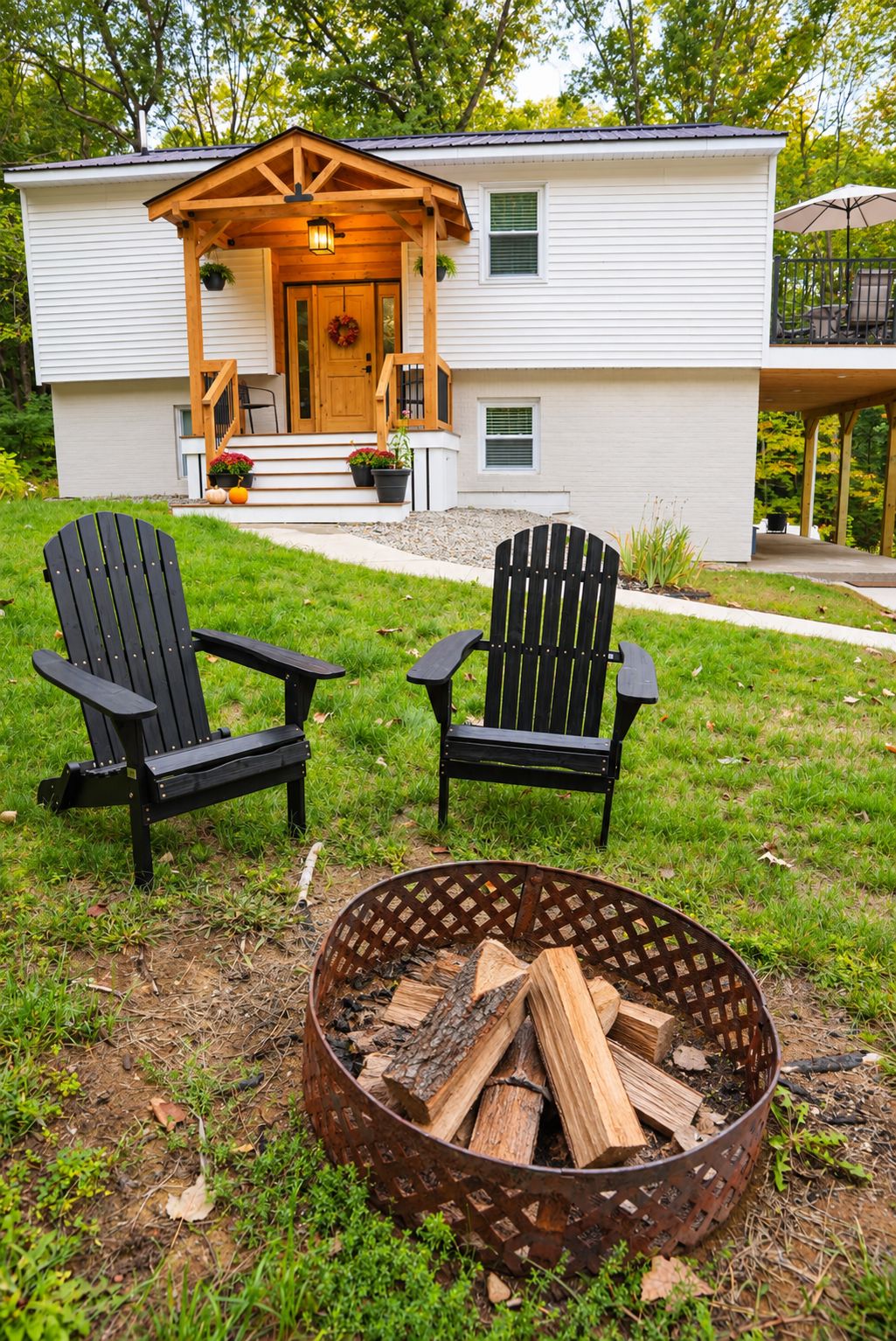 Ein Haus mit Veranda, zwei Adirondack-Stühlen und einem Feuerkorb mit Holz.