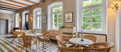 A room with checkered flooring, wicker furniture, and large windows with greenery outside.
