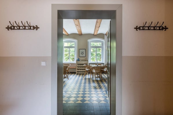A hallway with a checkered floor leading to a dining area with wicker furniture and a painting on the wall.