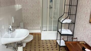 Ein Badezimmer mit Waschbecken, Toilette, Dusche und einer hölzernen Sitzbank.