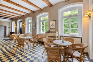 A room with checkered flooring, wicker furniture, and large windows with greenery outside.