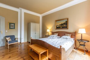 A bedroom with a wooden bed, a bench, a chair, a wardrobe, and two bedside lamps.