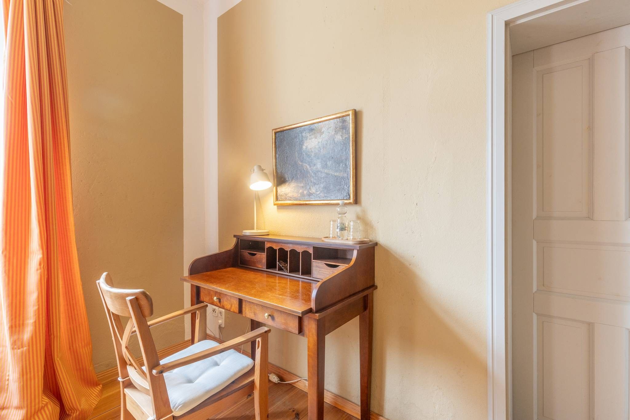Une pièce avec un bureau en bois, une chaise, une lampe et un tableau au mur.