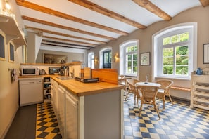Una cocina con encimera de madera, un comedor con sillas de mimbre y un suelo de cuadros.