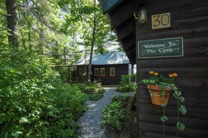 A wooden cabin with a gravel path leading to it, surrounded by lush greenery. - NEW FOR 2027: Secluded Lakefront Cabin w/ Incredible Beach on Pleasant Lake (Otisfield)