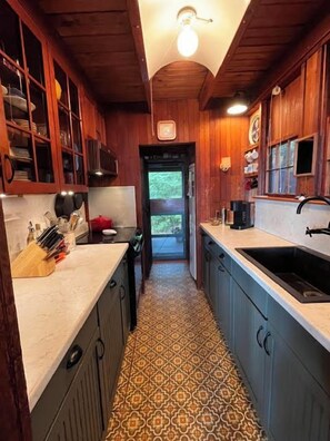 A narrow kitchen with wooden cabinets, a patterned floor, and a view into the dining area. - NEW FOR 2027: Secluded Lakefront Cabin w/ Incredible Beach on Pleasant Lake (Otisfield)