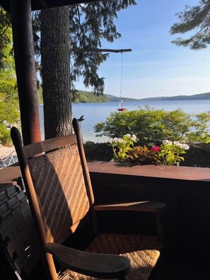 A wooden chair and table with a view of a lake and hills. - NEW FOR 2027: Secluded Lakefront Cabin w/ Incredible Beach on Pleasant Lake (Otisfield)