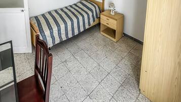 A small, sparsely furnished room with a bed, a nightstand, a chair, and a door.