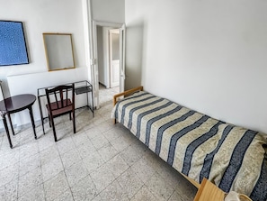 A dormitory room with a single bed, a chair, a table, and a mirror on the wall.