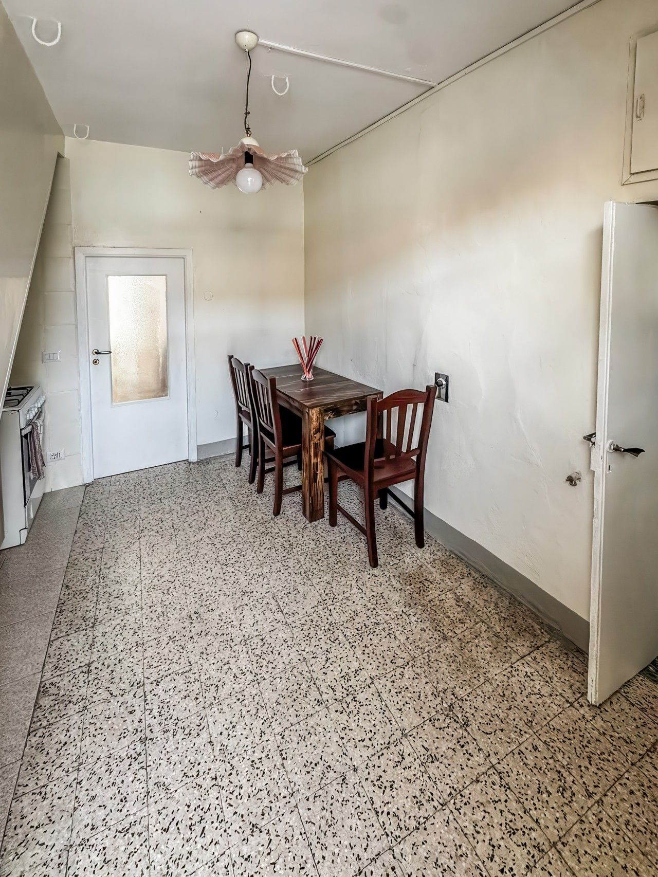 Uma área de refeições com mesa e cadeiras, um ventilador de teto, uma porta branca e piso de azulejos.