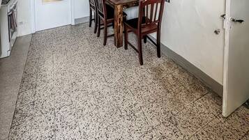 Uma área de refeições com mesa e cadeiras, um ventilador de teto, uma porta branca e piso de azulejos.