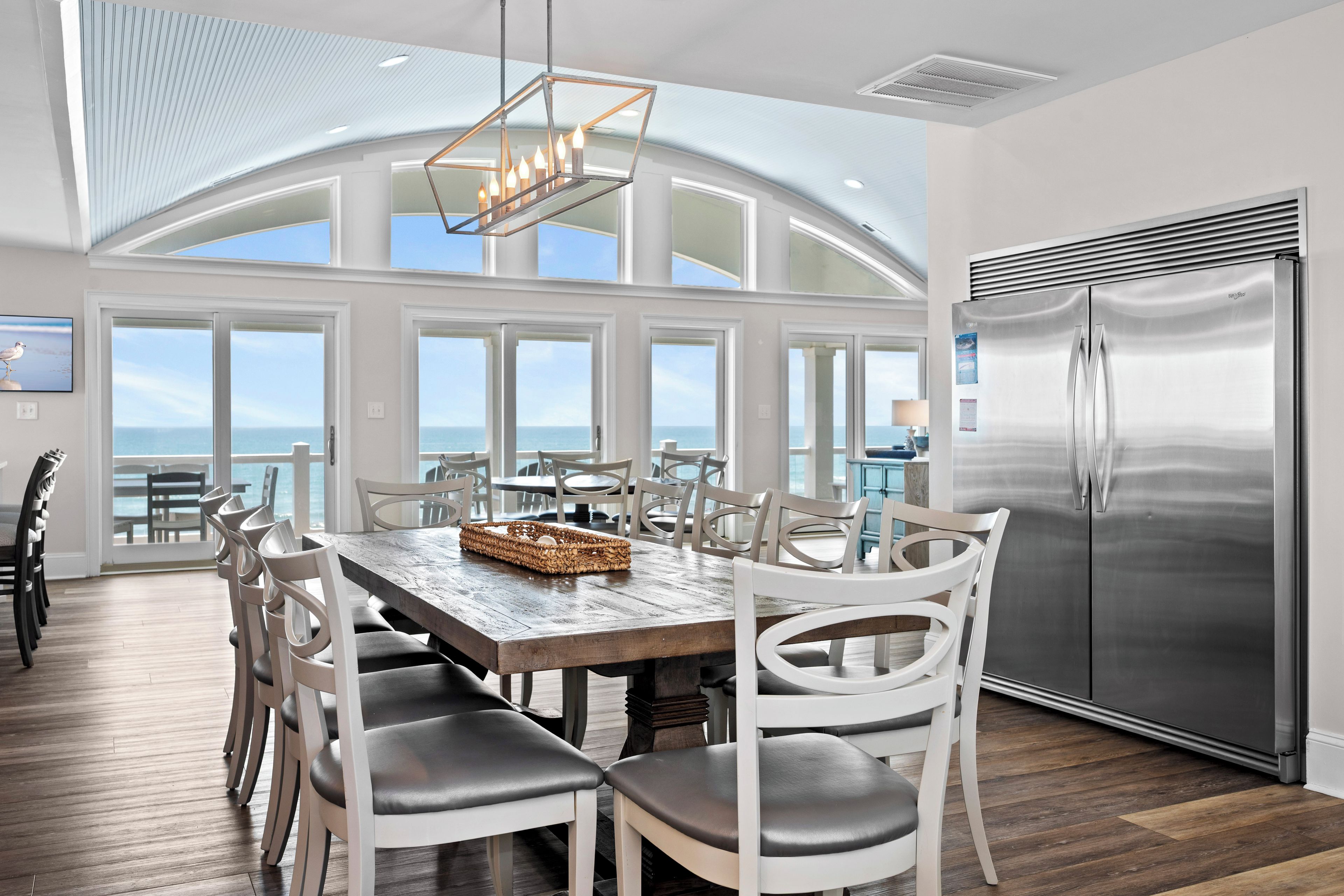 A spacious dining area with a large table, white chairs, and a view of the ocean.