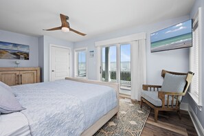 Ein Schlafzimmer mit einem Bett, einem Sessel, einem Deckenventilator, einem Fernseher und Blick auf den Ozean durch das Fenster.