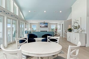 A spacious living area with a round table and chairs, a television, and a fireplace. - Oceanfront | 10 Bedrooms | Game Room | Pool | Theater (Emerald Isle)