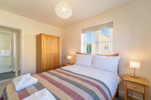 Une chambre à coucher comprenant un lit, une armoire en bois, une fenêtre avec des stores, une table de chevet avec une lampe et un lustre.
