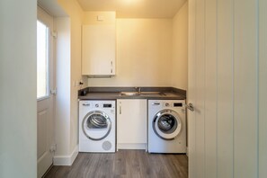 A compact laundry room with two Bosch washing machines, a sink, and a window. - Modern Home Near Blenheim Palace & The Cotswolds - Pass the Keys (Long Hanborough)