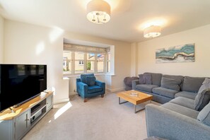 A living room with a flat-screen TV, a blue armchair, a grey sofa, a wooden coffee table, and a painting on the wall. - Modern Home Near Blenheim Palace & The Cotswolds - Pass the Keys (Long Hanborough)