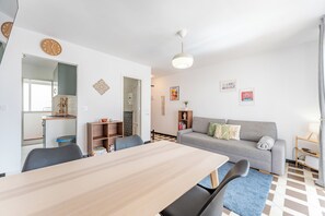 Ein modernes Wohnzimmer mit Esstisch, Sofa und sichtbarer Küchenzeile durch eine offene Tür.