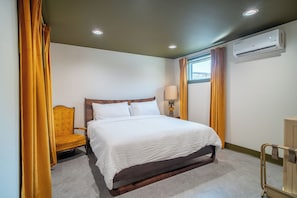 A hotel room with a bed, a chair, a lamp, and an air conditioning unit.