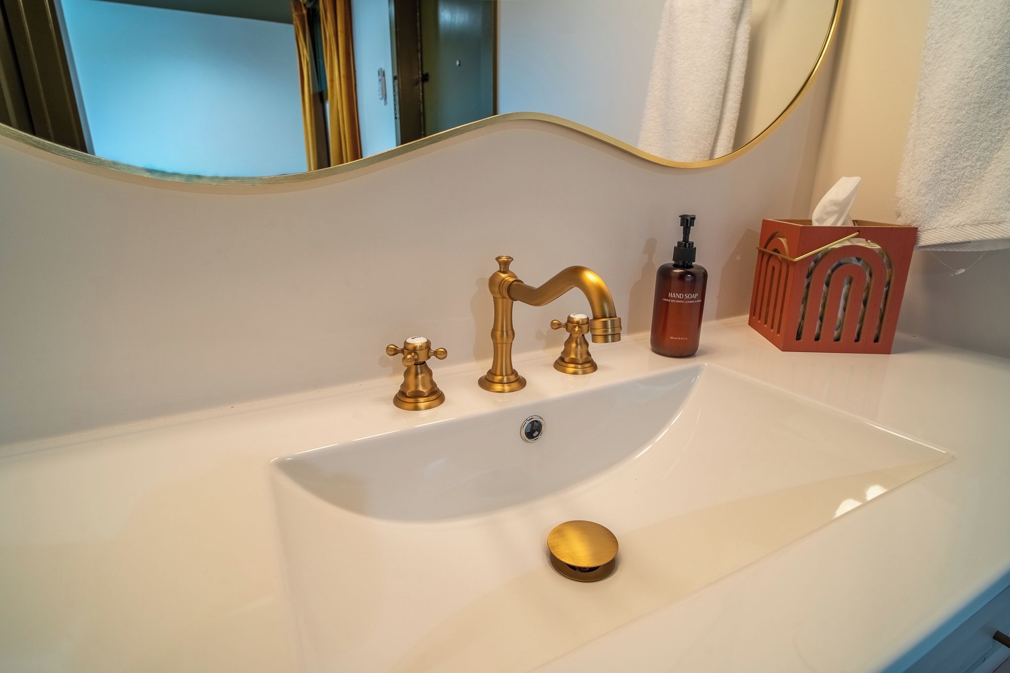 Une salle de bain avec un lavabo blanc, des robinets dorés, un distributeur de savon et un porte-serviettes.