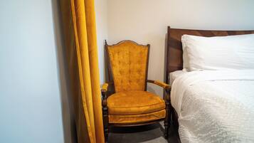 Quarto de hotel com cama de madeira, cadeira estofada amarela e cortina branca.