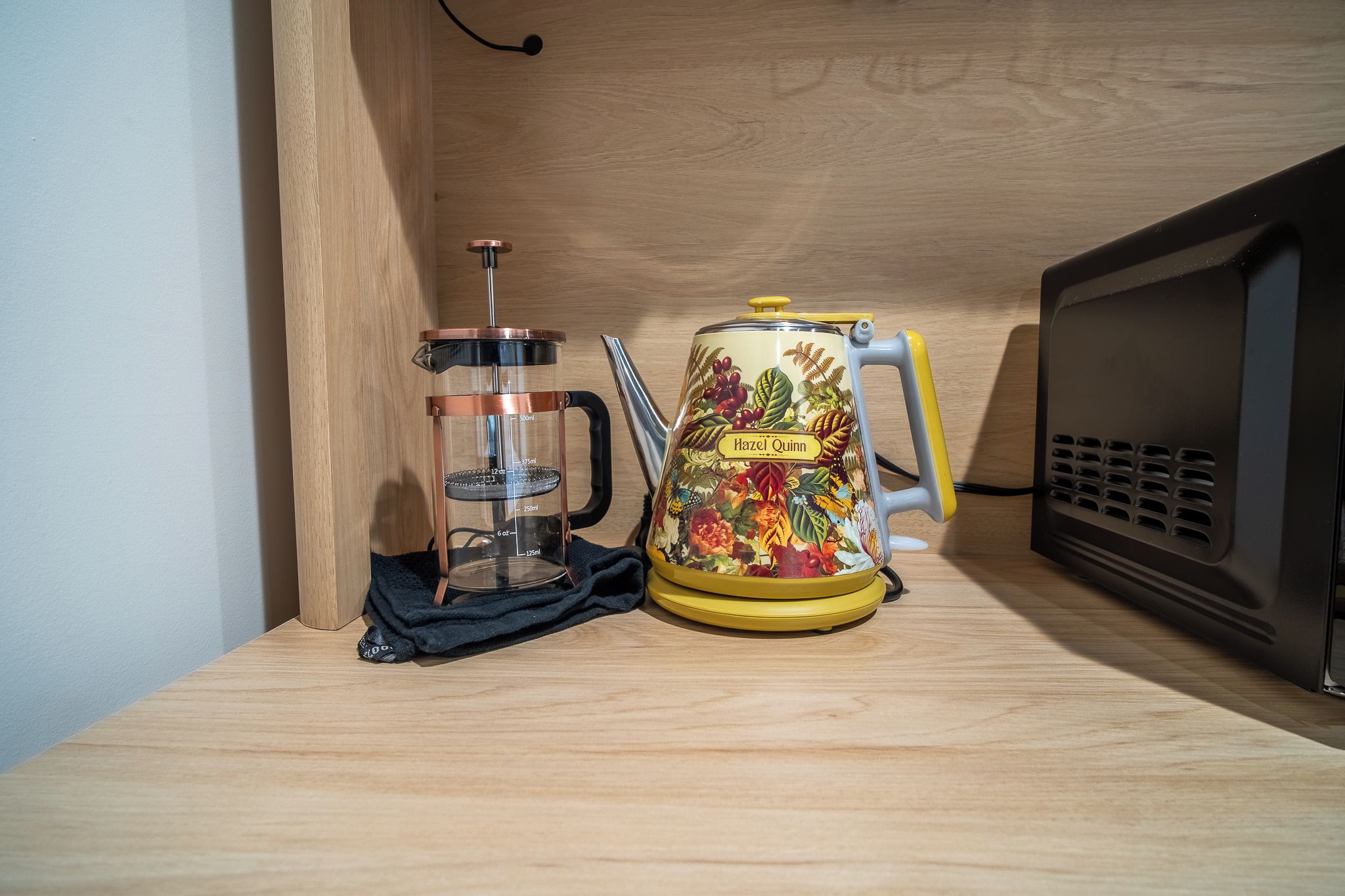 A kitchen with a coffee press, a kettle, and a microwave on a wooden countertop.