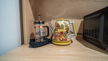 A kitchen with a coffee press, a kettle, and a microwave on a wooden countertop.