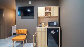 A compact kitchenette with a microwave, refrigerator, and a small shelf with items. A chair is placed in front of the kitchenette.