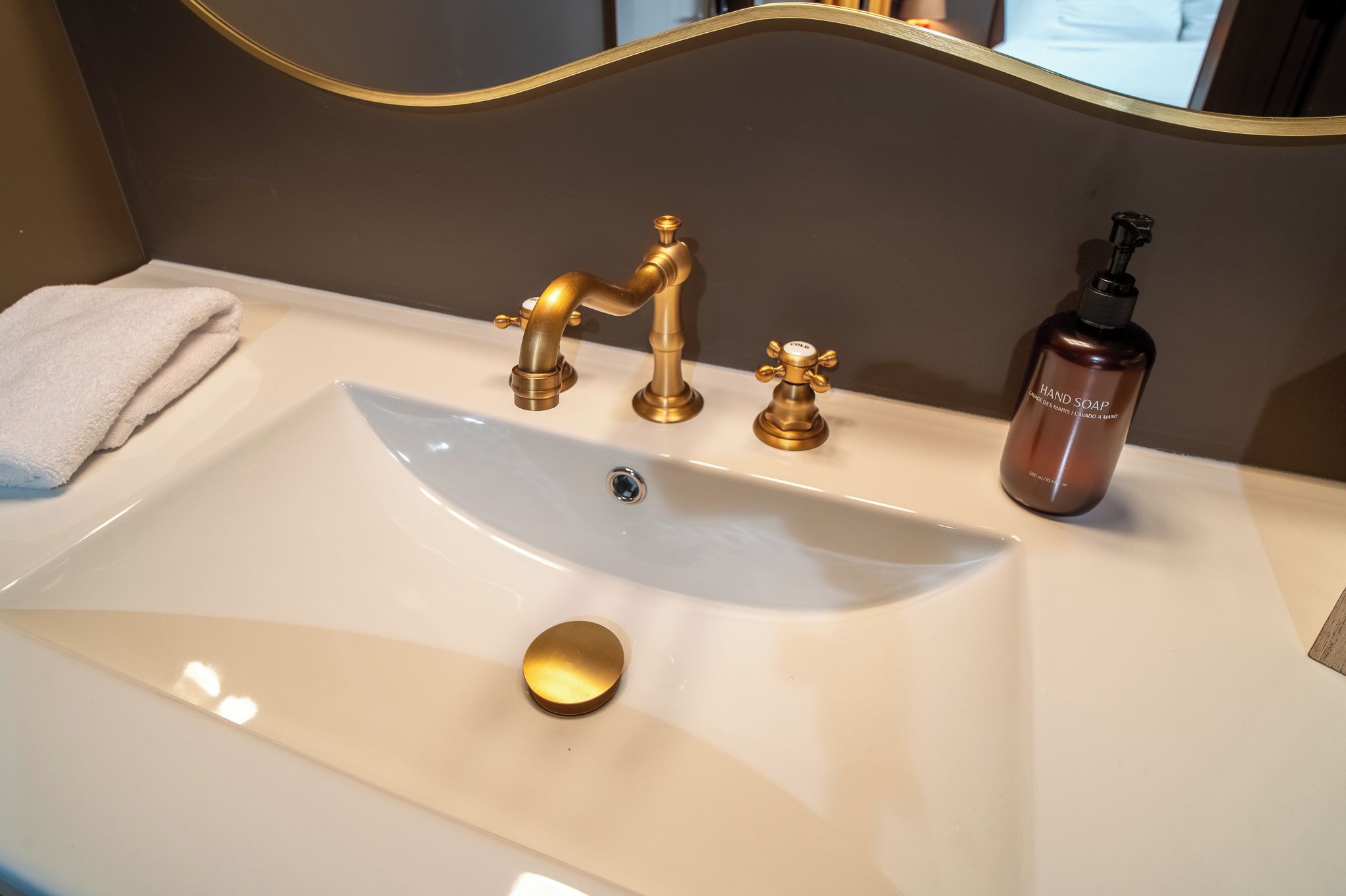 A bathroom sink with a gold faucet, a soap dispenser, and a towel.