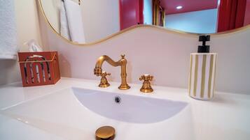 A bathroom with a white sink, gold faucets, a mirror, and a striped soap dispenser.