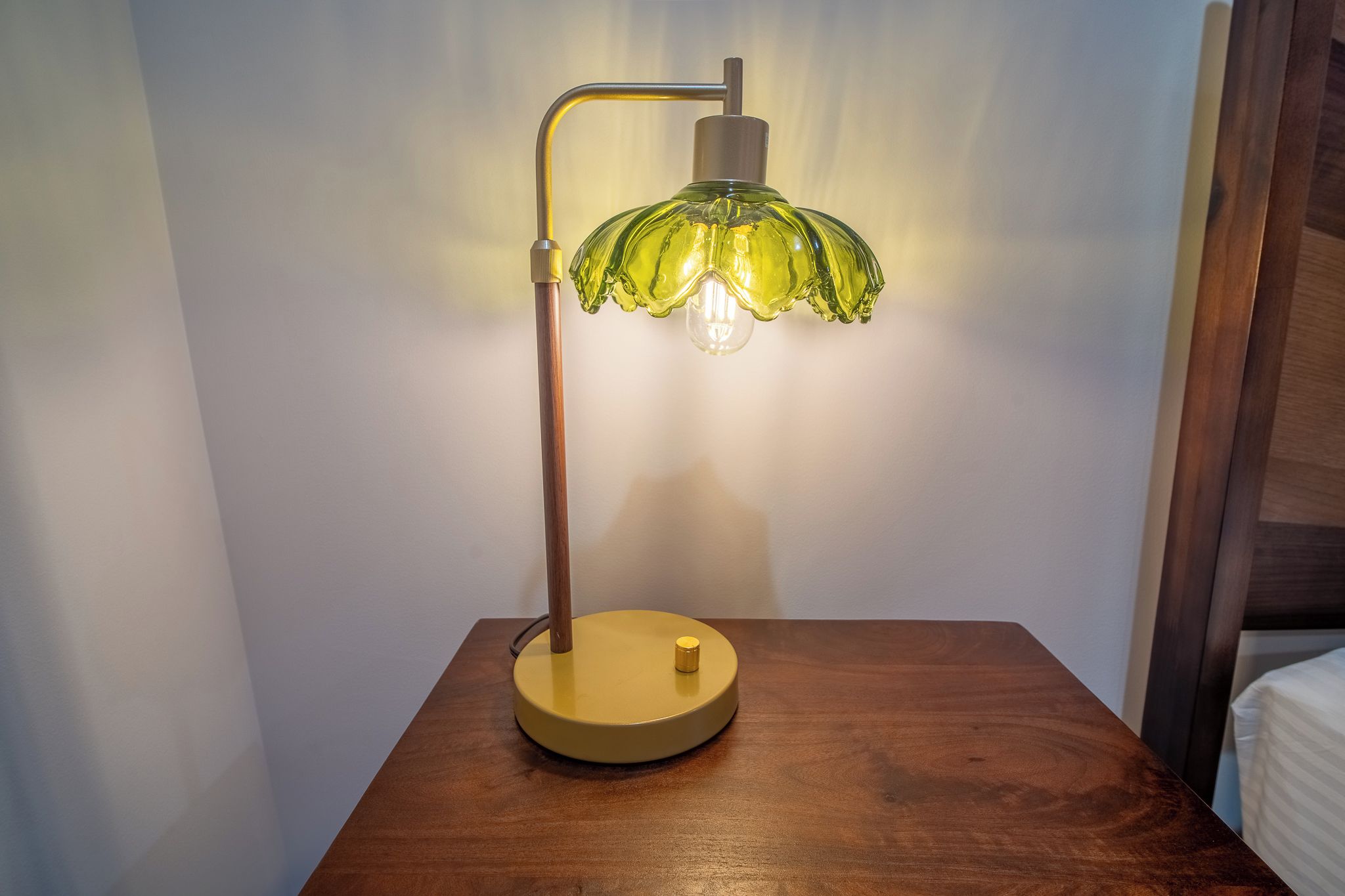 Uma luminária de mesa com base amarela e cúpula de vidro verde sobre uma mesa de madeira.
