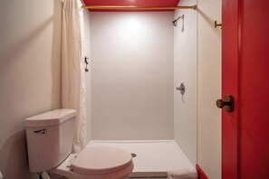 Un bany amb vàter, dutxa i una porta vermella.