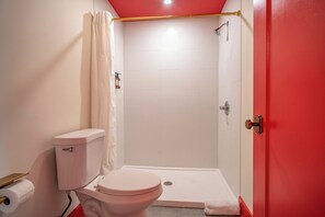 Un bany amb vàter, dutxa i una porta vermella.