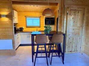 A wooden interior with a kitchen area featuring a table, chairs, a hanging light fixture, a window with blinds, and a door. - Enjoy peace and quiet, nature, and comfort in this cozy vacation home. (Waarland)