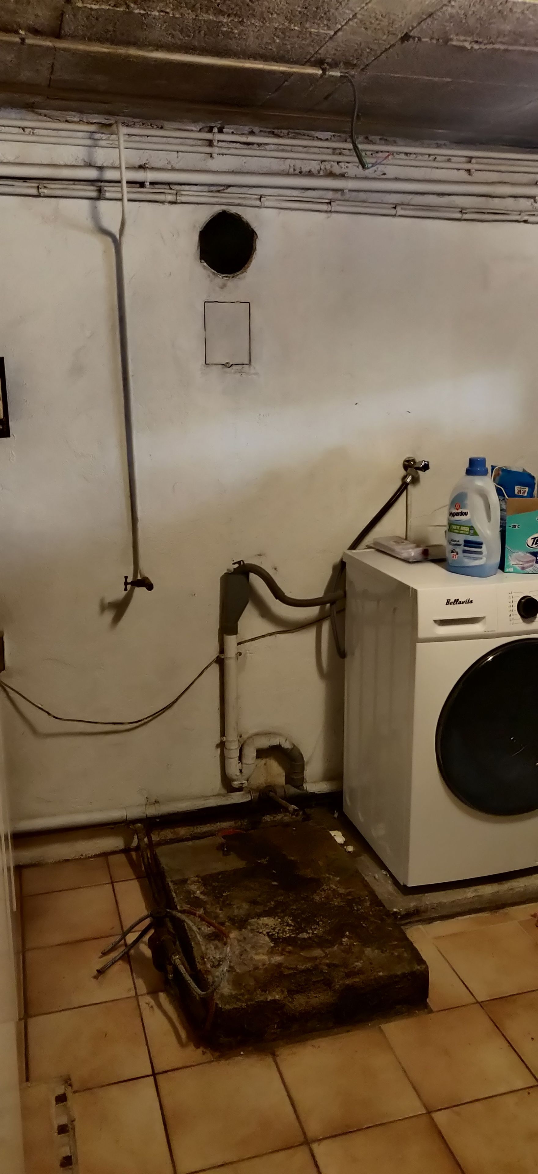 Une buanderie équipée d’un lave-linge, d’un chauffe-eau et d’une boîte en métal posée sur le sol.