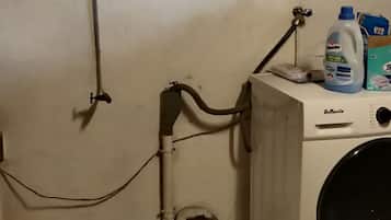 Une buanderie équipée d’un lave-linge, d’un chauffe-eau et d’une boîte en métal posée sur le sol.