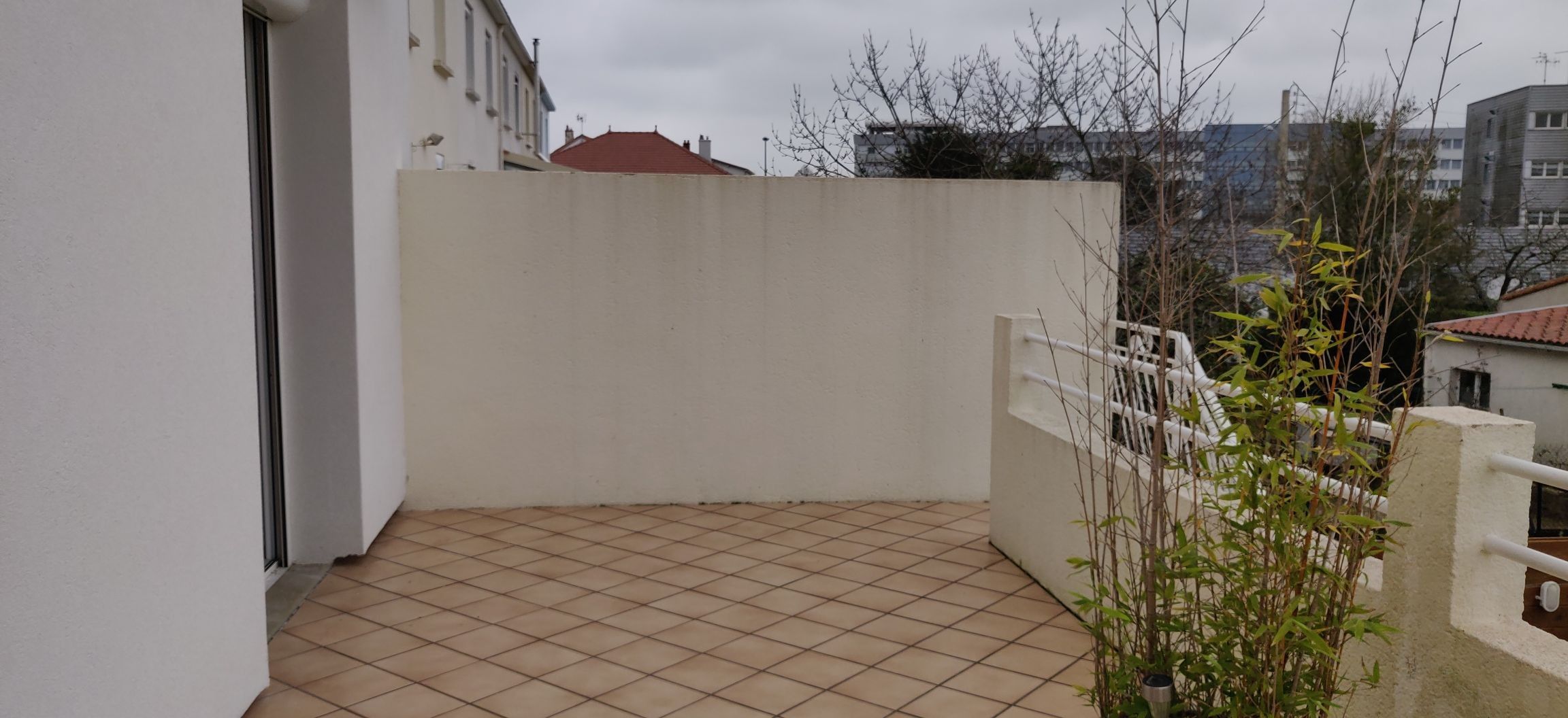 Uma varanda com piso de azulejos, parede branca e portão de metal.