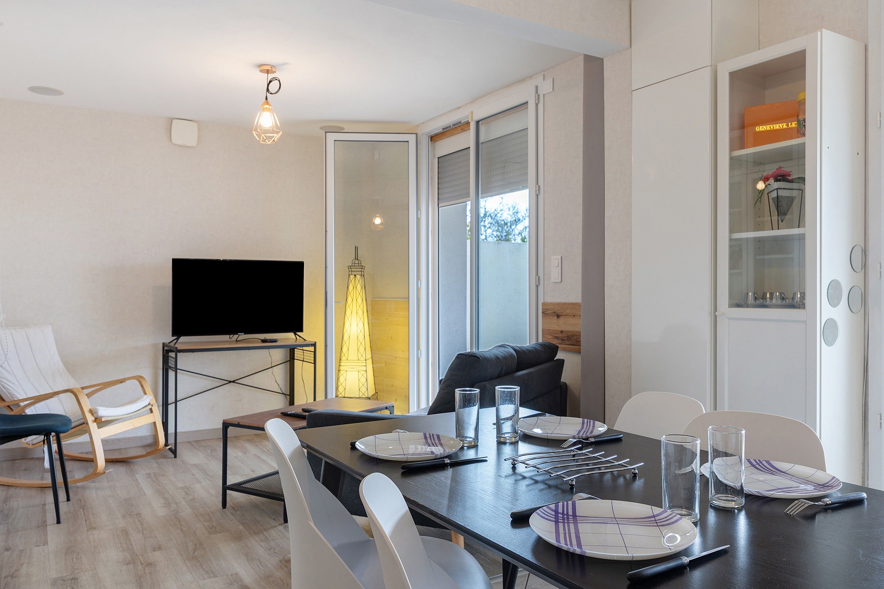 Een moderne eetruimte met een flatscreen televisie, een gedekte tafel voor twee personen en een bank op de achtergrond.