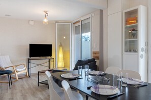 Un espace repas moderne avec un téléviseur à écran plat, une table à manger dressée pour deux personnes et un canapé en arrière-plan.