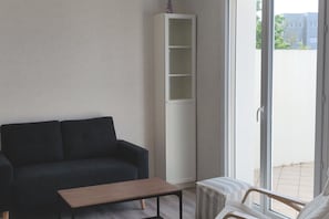 A living room with a dark sofa, a wooden coffee table, a white shelving unit, and a view of the outside through a sliding glass door.