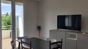 Ein Zimmer mit einem Fernseher auf einem Schrank, einem Esstisch mit Stühlen und einer Glasdoppeltür, die zu einem Außenbereich führt.