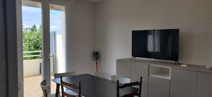 A room with a TV on a stand, a dining table with chairs, and a sliding glass door leading to an outdoor area.