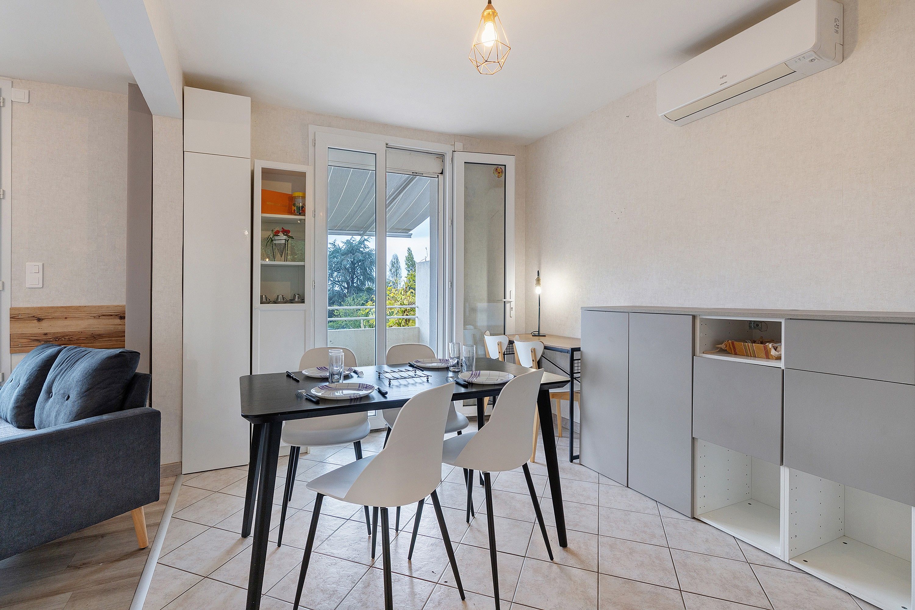 A modern kitchen with a dining area, white cabinetry, and a view through the glass door.