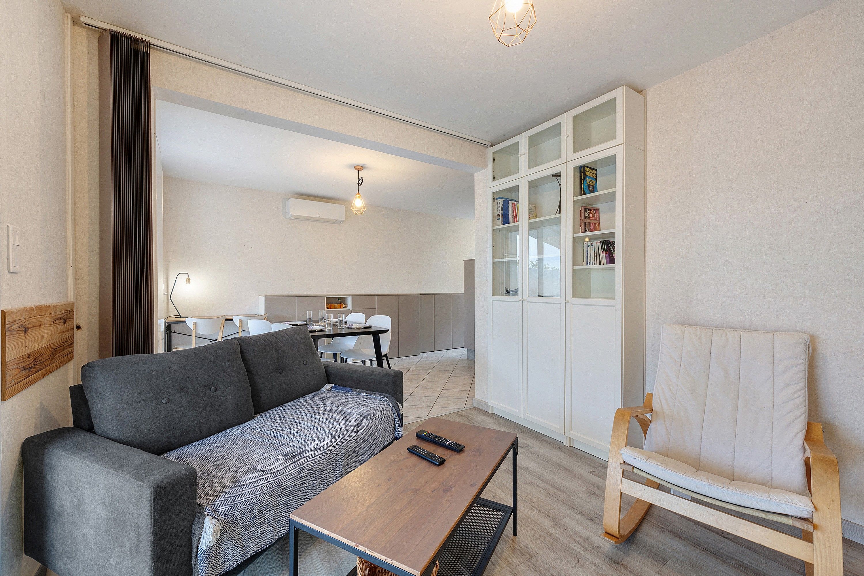 A modern living room with a sofa, a coffee table, a bookshelf, and a dining area with chairs and a table.